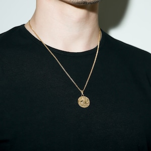 May include: A gold chain necklace with a round pendant featuring an intricate design. The pendant has a raised edge and appears to be made of metal.