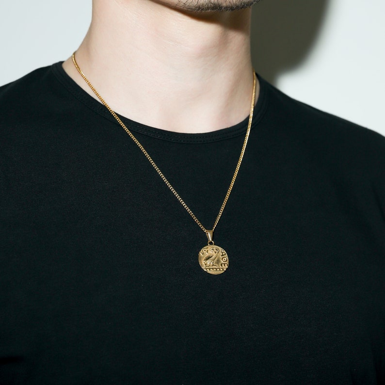 May include: A gold chain necklace with a round pendant featuring an intricate design. The pendant has a raised edge and appears to be made of metal.