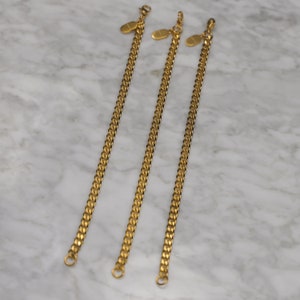 Peut inclure: Trois bracelets en cha&icirc;ne dor&eacute;s avec des fermoirs ovales. Les bracelets sont dispos&eacute;s en rang&eacute;e, le plus court &agrave; gauche et le plus long &agrave; droite.