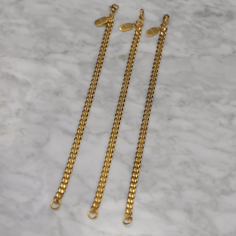 Peut inclure: Trois bracelets en cha&icirc;ne dor&eacute;s avec des fermoirs ovales. Les bracelets sont dispos&eacute;s en rang&eacute;e, le plus court &agrave; gauche et le plus long &agrave; droite.