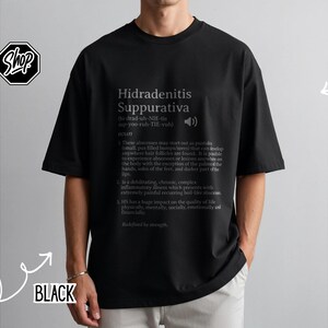 May include: Black t-shirt with the text "Hidradenitis Suppurativa" in a white, sans-serif font. The text includes a pronunciation guide and a definition of the condition. The shirt is a short-sleeved, oversized style.