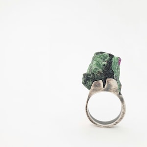 Può includere: Un anello d'argento con una pietra preziosa verde e nera incastonata nella fascia. La pietra preziosa ha un aspetto grezzo e naturale.