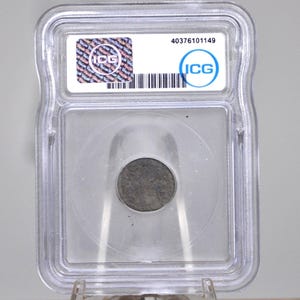 Op de afbeelding: Een donkere, ronde munt in een doorzichtige plastic houder. De houder heeft een wit label met de tekst "ICG" en een barcode. De munt is gecentreerd, wat duidt op een verzamelobject. Het nummer 40376101149.