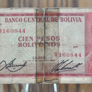 Peut inclure: Un billet de banque bolivien vintage avec un portrait d'un homme en uniforme militaire. Le billet est rouge, blanc et bleu avec le texte "Banco Central de Bolivia" et "Cien Pesos Bolivianos" imprimé dessus. Le billet porte le numéro de série "R160844".