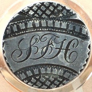 May include: A silver button with a decorative border and the initials "S & H" engraved in the centre.
