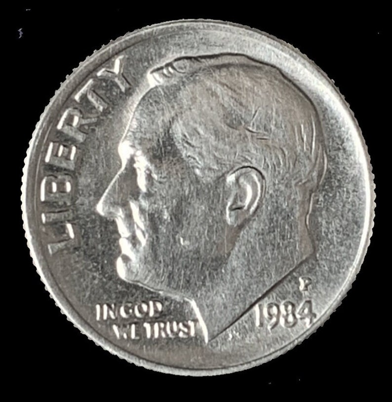 May include: A silver US dime coin with the inscription "LIBERTY" on the left side and "IN GOD WE TRUST" and "1984" on the bottom.