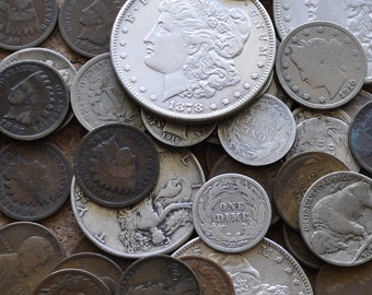 Op de afbeelding: Een verzameling vintage zilveren munten met verschillende ontwerpen, waaronder een Liberty Head-munt, een Native American-munt en een dime. De munten zijn willekeurig gerangschikt op een bruin oppervlak.