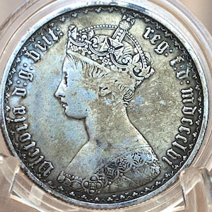 Puede incluir: Una moneda de plata con un retrato de la reina Victoria, con una corona, y la inscripción "Victoria D:G: Brit: Reg: F:D: 1861" alrededor del borde.
