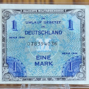 May include: A blue and white German banknote with the text "ALLIIERTE MILITÄRBEHÖRDE C" and "DEUTSCHLAND" printed on it. The banknote has a serial number "078394036" and the text "EINE MARK" printed on it.