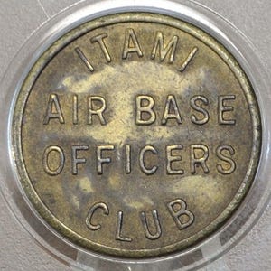 以下が含まれることがあります： 「ITAMI AIR BASE OFFICERS CLUB」と大文字で刻まれた、丸い真鍮製のコイン。 コインは透明なプラスチックホルダーに入っています。 コインは使い古された、古びた外観をしています。