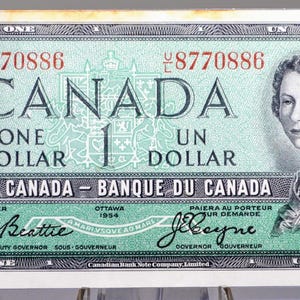 以下が含まれることがあります： 1954年のカナダ1ドル紙幣。女性の肖像と「CANADA」の文字が特徴です。紙幣は緑とグレーを基調とし、「ONE DOLLAR」と「BANK OF CANADA」の文字が印刷されています。