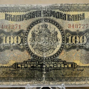 May include: A vintage 100 Bulgarian leva banknote. The note features text in Cyrillic script, the denomination "100", and a central emblem. The note is primarily tan and gray, with intricate designs and serial numbers.