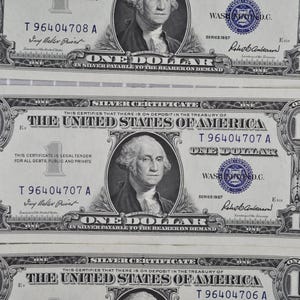 Pode incluir: Três certificados de prata de um dólar. Cada nota apresenta um retrato de George Washington e o texto "ONE DOLLAR". As notas são da Série de 1957.