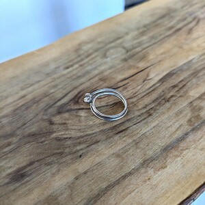 May include: Two silver rings stacked on top of each other on a wooden surface.