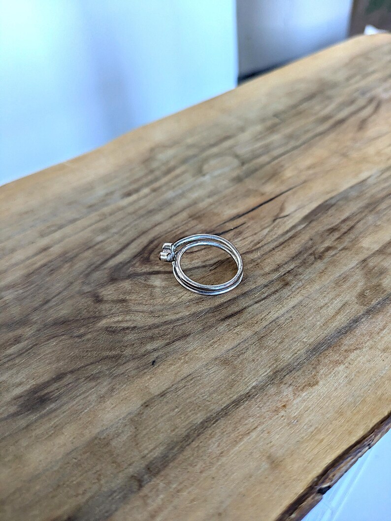 May include: Two silver rings stacked on top of each other on a wooden surface.
