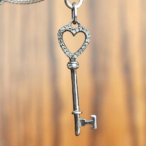 May include: A silver key pendant necklace with a heart-shaped keyhole and a row of clear cubic zirconia stones around the edge.