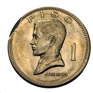 Puede incluir: Una moneda de color dorado con la palabra "PISO" en la parte superior y el número "1" a la derecha. La moneda presenta un perfil de un hombre y el nombre "JOSE RIZAL" en la parte inferior. La moneda tiene un borde texturizado.