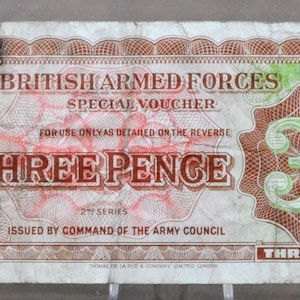 May include: A vintage British Armed Forces Special Voucher for Three Pence. The voucher features text in red and green, with the denomination in the corners and a large "3d" in the center. The text reads "Issued by Command of the Army Council."