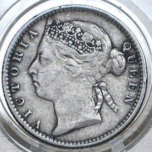 May include: A silver coin depicting Queen Victoria in profile, crowned and with a bun. The coin is in a clear protective case. The words "VICTORIA QUEEN" are inscribed around the edge of the coin.