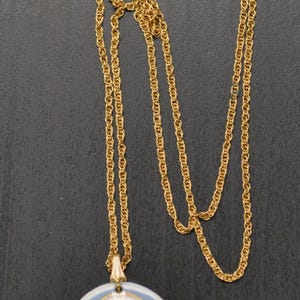 May include: A gold chain necklace with a porcelain pendant featuring a floral design. The pendant is oval shaped and has a blue background with white and pink flowers.