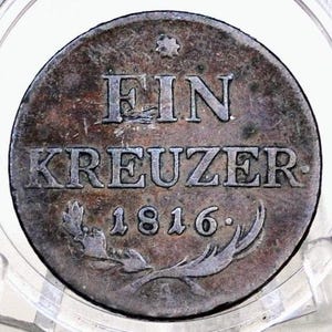May include: A silver coin with the inscription "EIN KREUZER 1816." The coin has a wreath design on the bottom.