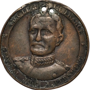 May include: A circular bronze-toned metal medallion featuring a relief portrait of a man in a military uniform. The text OUR LEADER IN FRANCE is embossed along the top edge, and GENERAL JOHN J. PERSHING is embossed along the bottom edge.