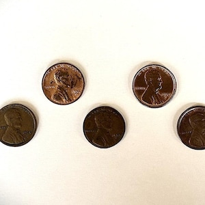 以下が含まれることがあります： 銅色の米国1セント硬貨（ペニー）6枚が互い違いに配置されています。各硬貨には右を向いたエイブラハム・リンカーンの横顔が描かれており、「Liberty」、発行年、および「In God We Trust」というモットーが刻まれています。