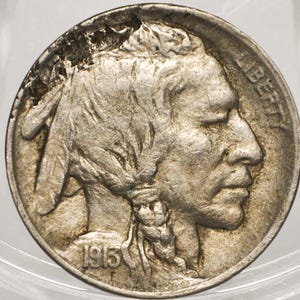 Op de afbeelding: Een zilverkleurige 1913 Buffalo nikkelmunt met het profiel van een inheemse Amerikaanse figuur die naar rechts kijkt. Het woord LIBERTY staat langs de rechterbovenrand en het jaartal 1913 is zichtbaar linksonder op de ronde munt.