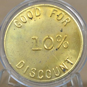 Peut inclure: Une pièce de monnaie dorée avec les mots "GOOD FOR" en haut et "DISCOUNT" en bas. Le nombre "10%" est au centre. La pièce est enfermée dans un support en plastique transparent.