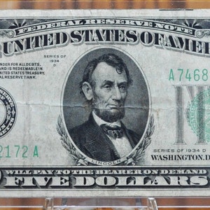 May include: A five dollar bill from the Federal Reserve Note series of 1934 D, featuring a portrait of Abraham Lincoln and the text "WILL PAY TO THE BEARER ON DEMAND FIVE DOLLARS".