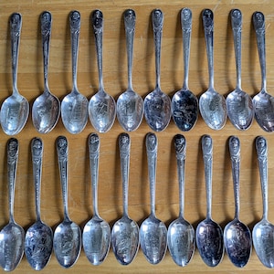 Puede incluir: Colección de cucharas de plata antiguas dispuestas sobre una superficie de madera. Cada cuchara presenta un diseño detallado en el mango y el cuenco. La disposición resalta la intrincada artesanía y el encanto vintage de las cucharas.