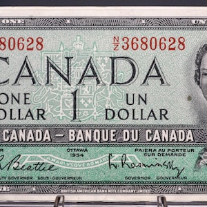 以下が含まれることがあります： 1954年のカナダ1ドル紙幣。緑とグレーを基調とし、「CANADA」と「ONE DOLLAR」の文字が記されています。右側には女性の肖像画が描かれています。シリアルナンバーも確認できます。サイズは適用されません。