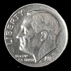 May include: A silver US dime coin with the inscription "LIBERTY" on the left side and "IN GOD WE TRUST" and "1982" on the bottom.