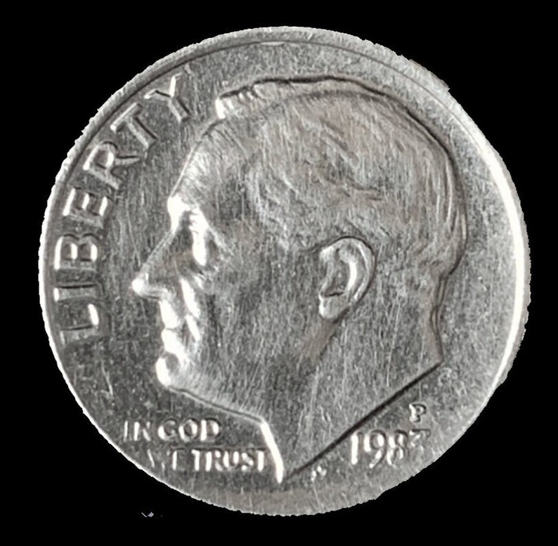 May include: A silver US dime coin with the inscription "LIBERTY" on the left side and "IN GOD WE TRUST" and "1982" on the bottom.