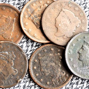 May include: A collection of six vintage copper large cent coins featuring the profile of Lady Liberty, with visible dates including 1841, 1848, and 1837. Each coin displays a circular design with stars along the rim and aged, weathered metal surfaces.