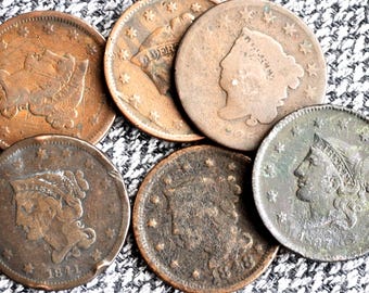 May include: A collection of six vintage copper large cent coins featuring the profile of Lady Liberty, with visible dates including 1841, 1848, and 1837. Each coin displays a circular design with stars along the rim and aged, weathered metal surfaces.