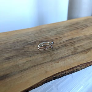 May include: A silver ring with a delicate design. The ring is made of two bands that are intertwined and have a small, round stone set in the center.