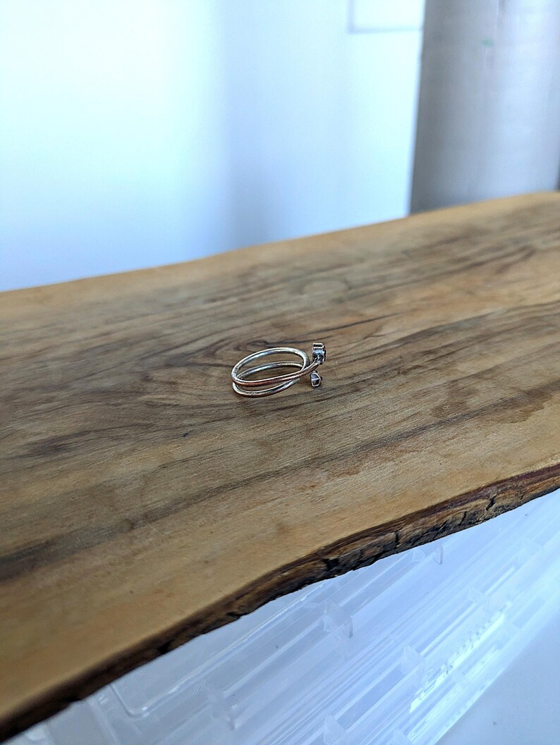 May include: A silver ring with a delicate design. The ring is made of two bands that are intertwined and have a small, round stone set in the center.