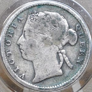 May include: A silver coin featuring a profile of a woman with the inscription "VICTORIA QUEEN" around the edge. The coin is encased in a clear protective holder, showcasing its details.