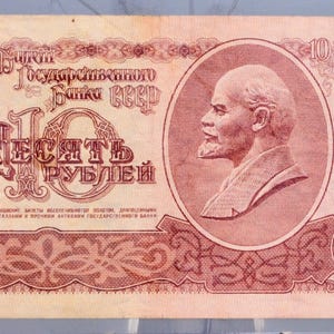 May include: A vintage 10-ruble banknote from 1961, featuring a portrait of a man on the right and the Soviet coat of arms on the left. The note is predominantly red with intricate designs and Cyrillic text.