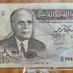 Op de afbeelding: Een Tunesisch bankbiljet van vijf dinar met een portret van Habib Bourguiba, de eerste president van Tunesië, met de tekst "البنك المركزي التونسي" (De Centrale Bank van Tunesië) en "خمسة دنانير" (Vijf Dinar) gedrukt op het biljet.