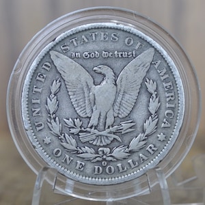 May include: A silver dollar coin with an eagle design. The coin has the words "United States of America" and "In God We Trust" inscribed on it. The coin also has the words "One Dollar" inscribed on it.