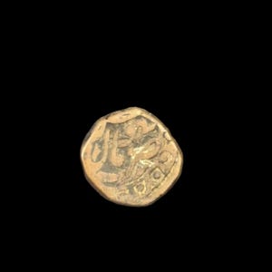 Op de afbeelding: Een goudkleurige, antieke munt met ingewikkelde reliëfontwerpen. De munt heeft gestileerde letters en symbolen, mogelijk van historische betekenis. De munt staat tegen een zwarte achtergrond, waardoor de details worden benadrukt.