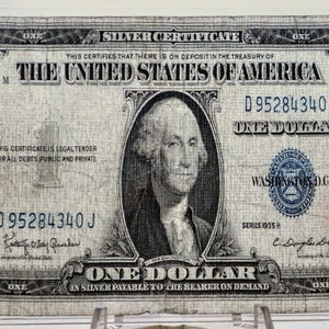 May include: A vintage one-dollar silver certificate from the United States, featuring a portrait of George Washington. The bill is predominantly gray and black, with text including "Silver Certificate" and "One Dollar."