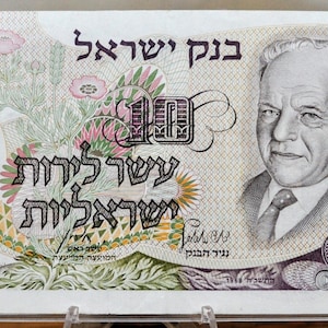 May include: A ten Israeli lira banknote featuring a portrait of a man in a suit and tie. The bill has Hebrew text and floral designs in pink, green, and yellow. The number 10 is displayed in multiple locations.