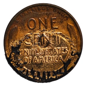 Könnte beinhalten: Eine kupferfarbene Ein-Cent-Münze aus den Vereinigten Staaten mit dem Text E PLURIBUS UNUM oben, ONE CENT in der Mitte und UNITED STATES OF AMERICA unten. Die Münze weist deutliche Oberflächenschäden, dunkle Verfärbungen und starken Abrieb auf.