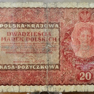 Puede incluir: Un billete polaco antiguo, predominantemente rojo y beige, con patrones y texto intrincados. El billete presenta un retrato dentro de un marco decorativo, la denominación "20" en rojo y el texto "POLSKA KRAJOWA".