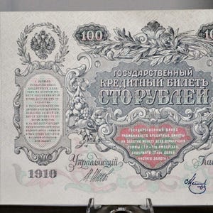 Peut inclure: Un billet de banque russe de 100 roubles de 1910. Il présente des inscriptions en cyrillique, le chiffre "100" et des motifs ornementaux. La palette de couleurs est rouge et verte.