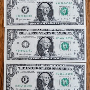May include: Three one-dollar bills from the United States of America, each featuring a portrait of George Washington in the center, the text Federal Reserve Note, and serial numbers H34641038C, H34641039C, and H34641040C printed in green ink.