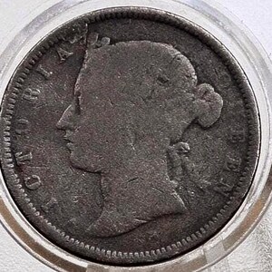 May include: A close-up of an antique coin encased in a clear protective holder. The coin features a profile of a woman's head and the word "VICTORIA" around the edge. The coin is a dark, aged color.